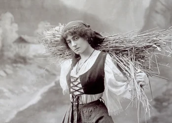 Young woman in traditional dress carrying a bundle of straw