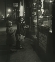 Two Little Girls in Winter Coats Standing Outside a Shop at Night