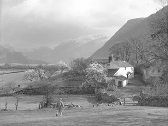 A man walking towards a lane and Gillerthwaite House, with lake and hills in background