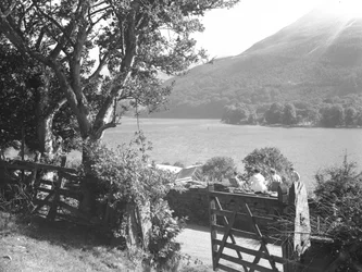 Four people having a picnic on a dry stone wall overlooking a lake, car parked with boot open