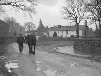 Man leading horse down road toward village buildings and church