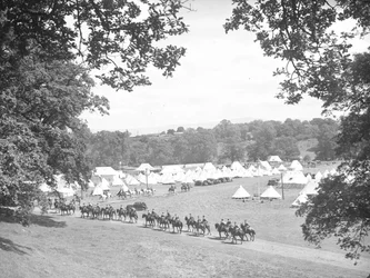 Mounted cavalry moving along road towards their camp with tents in the background