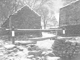 Stone slab bridge and handrail crossing stream with farm buildings behind