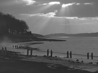 View of estuary looking towards the sea; seascape; with old jetty posts in foreground and children on mud flats in distance