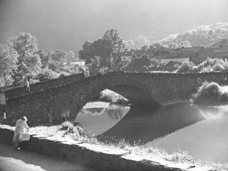 Woman sitting on wall studying map with river and stone bridge in background