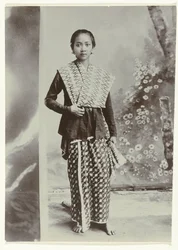 Studio portrait of a young Javanese woman in a sarong with batik motif and a checkered shirt