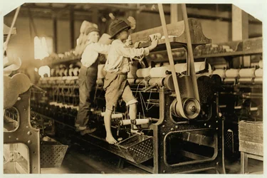 Small boys climbing on spinning frame to mend broken threads and replace empty bobbins at Bibb Mill, Macon, Georgia, 1909