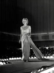 Model photographed on a runway in evening dress with rhinestone shoulder straps; the article is a creation of the couture house 