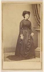 [Unidentified woman wearing a hat and long dark dress.]