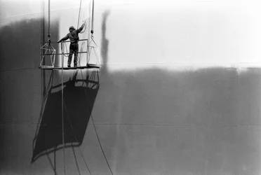 Man on platform painting an oil storage tank