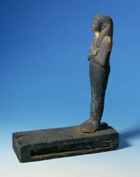 Ptah-Sokar-Osiris figure with tripartite wig and crossed arms on a rectangular plinth with a compartment containing a section of papyrus, Egyptian, 21st-22nd Dynasty, c.900 BC