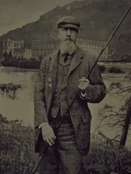 Studio portrait of 8th Duke of Devonshire in tweeds holding fishing rod in front of a printed screen depicting Chatsworth