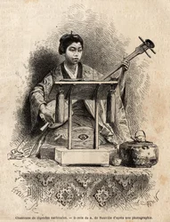 A singer of national legends, playing shamisen to accompany her song, sitting behind her desk. Engraving to illustrate the voyage to Japan, in 1863-1864, by Aimé Humbert, minister of the Swiss Confederation, in "Le Tour du monde, nouveau journal des