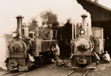 Two steam locomotives being maintained by two workers
