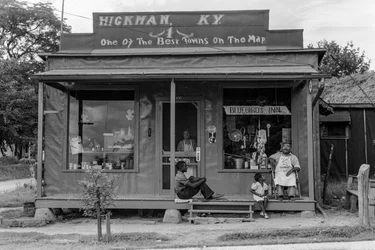African-American men and child relax on the porch of a tiny general store on the edge