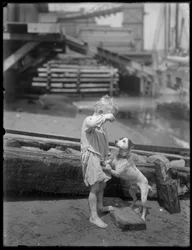 Barefoot boy, possibly William Gray Hassler, plays with dog on the shore of a river or lake, New York, c.1910