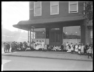 Children pose in front of an unidentified storefront branch of the Queens Borough Public Library, New York, c.1910