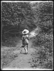 William Gray Hassler in Straw Hat and Overalls, Carrying Fishing Pole and Basket, Walking Down a Path in the Woods Alone, August 20, 1911